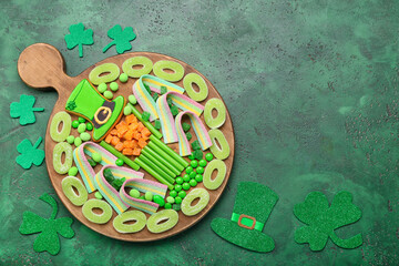 Wooden board with different sweets for St. Patrick's Day celebration on green background