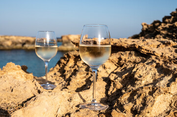 Two glasses of cold white dry white wine served on rocks in blue sea bay near Protaras touristic town on Cyprus