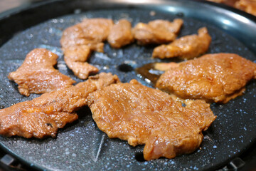 Seasoned pork is being grilled on a black grill.