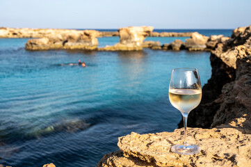 Glass of cold white dry white wine served on rocks in blue sea bay near Protaras touristic town on Cyprus