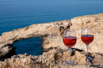 Two glasses of rose dry white wine served on rocks in blue sea bay with Love Bridge on background near Ayia Napa touristic town on Cyprus