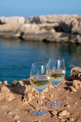 Two glasses of white dry white wine served on rocks in blue sea bay near Protaras touristic town on Cyprus