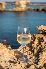 Glass of cold white dry white wine served on rocks in blue sea bay near Protaras touristic town on Cyprus