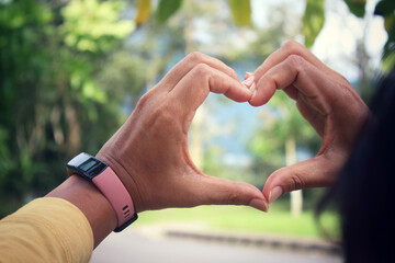 Hands of the person in the shape of heart. Woman making and showing love valentine symbol with hand gesture on blurry garden view background.