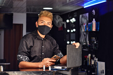 un joven empresario posa en su barbería mientras atiende virtualmente a sus clientes para agendarles los cortes de pelo el mismo día 