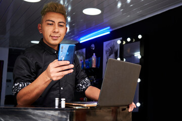 joven peluquero recibiendo citas en su teléfono inteligente y agendado a sus clientes en su computadora 