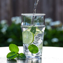 Pouring Fresh Water with Lime and Mint on Ice Out in the Garden