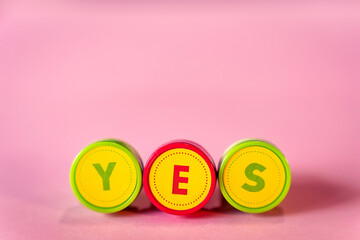 Word YES in letters text from kid's toy stamps isolated on a pink background