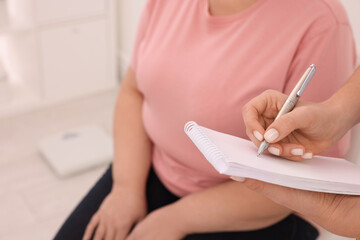 Nutritionist with notebook consulting overweight woman in clinic, closeup