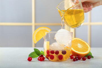 Woman pouring tasty cocktail into glass with ice balls at light grey marble table, closeup