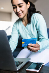 young hispanic woman using credit card while checking online bank account over laptop at home in Mexico Latin America
