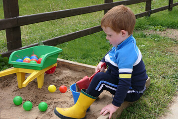 Red headed Child playing with toys in Sand Pit