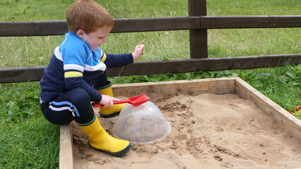 Red headed Child playing with toys in Sand Pit