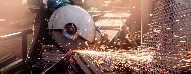 Banner Industry worker working electric wheel grinding on steel structure in factory, light spark