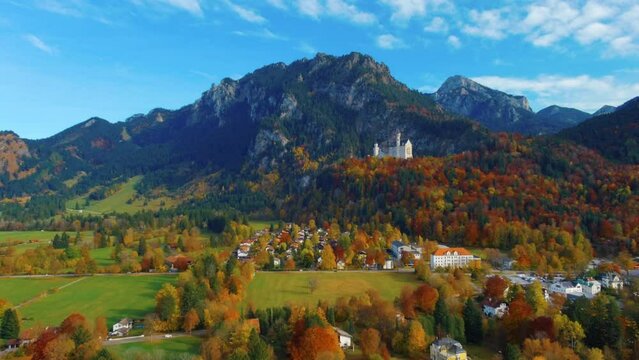 Relaxing view of drone lowering down towards village houses towards castle on hill over scenic autumn field in the afternoon near the Neuschwanstein Castle in Germany, Europe, wide view