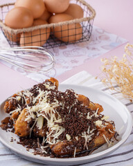 Fried Banana or Pisang goreng  served on white plate with topping chocolate Sprinkles and cheese. Pisang goreng  Is popular street food in South East Asia, especially in Malaysia and Indonesia.