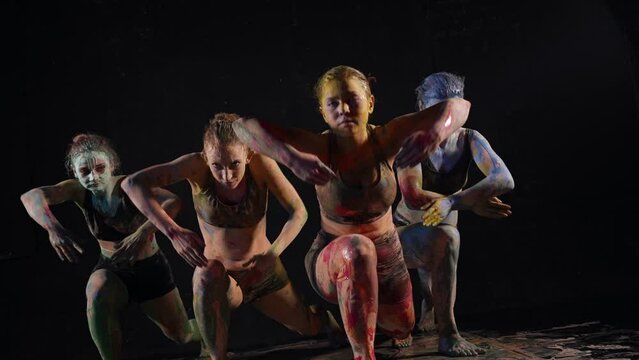 unusual dance performance with paints, women are covered by dyes are dancing together in darkness
