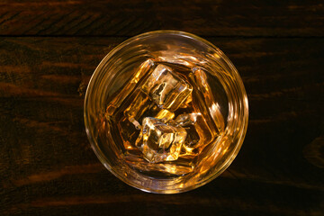 Close-up view of a glass of whiskey and ice on a dark wooden background.