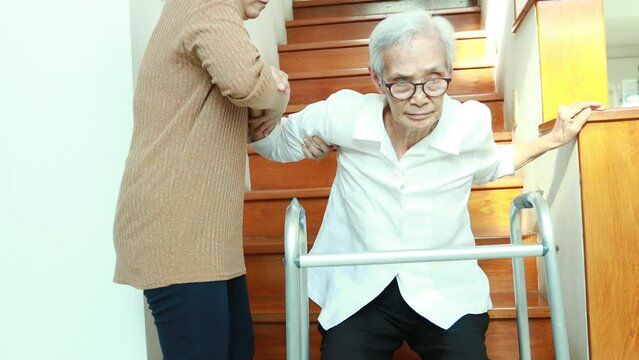 Asian caregiver helping a senior woman who sits on the floor of a staircase after she has dizziness,lift her up,help support to stand up and walk safely at nursing home,concept of health care,service