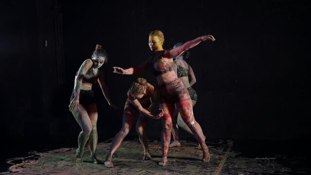 alluring women are dancing in dark studio, female bodies are covered by paints, slow motion