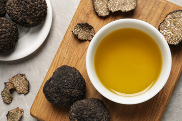 Fresh truffles and oil in bowl on light grey table, flat lay