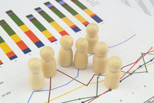 People and economy, demography and statistics concept. Wooden people figures on financial diagram and graphs.
