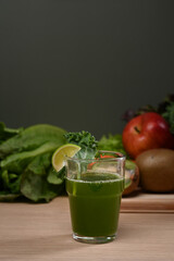 Green healthy juice with organic fruits and vegetables on wooden table.