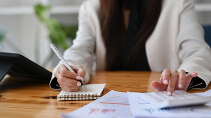 Female accountant making notes on notebook and using calculator at office desk.