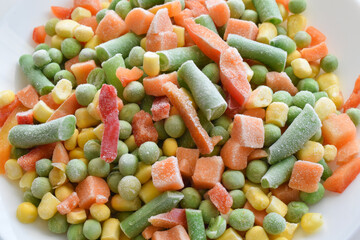 Frozen vegetables included carrot, green beans, peas and corn or maize on a white plate.