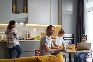 Man sitting before laptop in kitchen with family