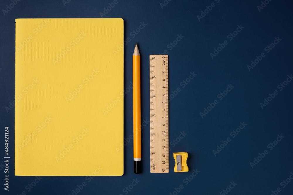 Poster top view pastel yellow notebook with yellow pencil and notepad on navy blue working table
