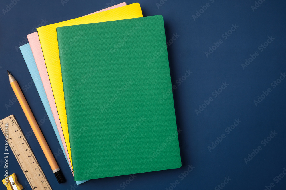 Poster top view pastel notebook with yellow pencil and notepad on navy blue working table