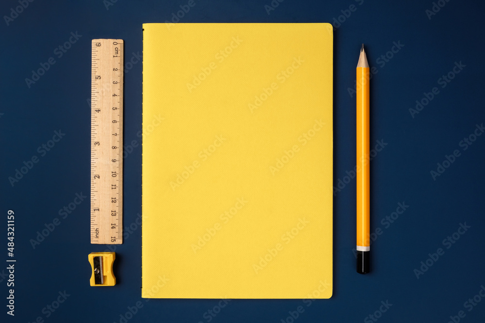 Poster top view pastel yellow notebook with yellow pencil and notepad on navy blue working table