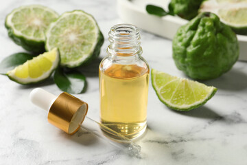 Bottle of essential oil, pipette and fresh bergamot fruits on white marble table