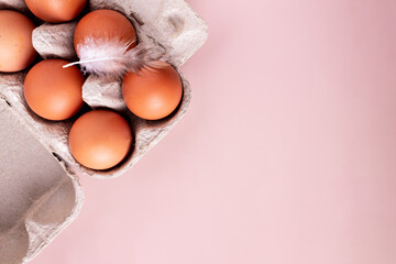 chicken eggs and a feather lie in a cardboard box on a beige background, copy space © Rara