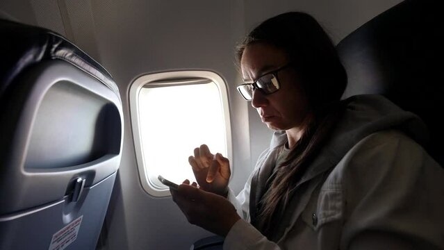 woman is using smartphone inside plane during flight, travelling by airplane