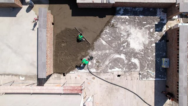 Aerial view of man builder screeding floor on the roof of residential building. Another man leveling surface with straight edge while screeding floor outdoors in new building.