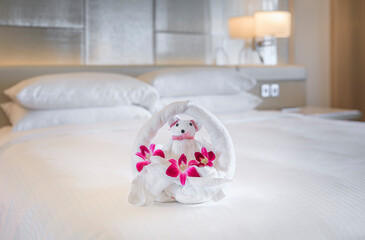 Hotel bed with towel art design shaped as a bear in a flower basket with orchids
