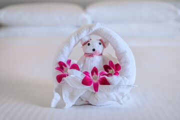 Fototapeta na wymiar Hotel bed with towel art design shaped as a bear in a flower basket with orchids