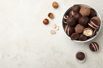 Different delicious chocolate truffles in bowl on light grey table, flat lay. Space for text