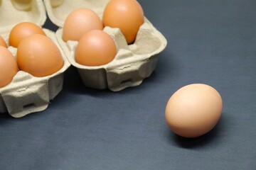Cardboard egg boxes with seven brown eggs on a black background, but one egg is outside the box.