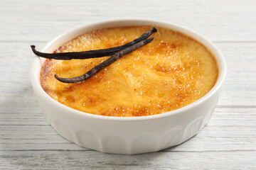 Delicious creme brulee and vanilla sticks on white wooden table, closeup view