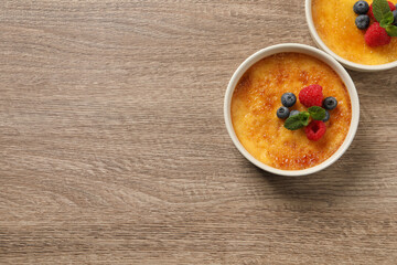 Delicious creme brulee with fresh berries on wooden table, flat lay. Space for text