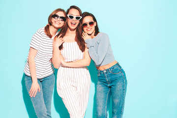 Three young beautiful smiling hipster female in trendy summer clothes.Sexy carefree women posing near blue wall in studio.Positive models in sunglasses. Cheerful and happy