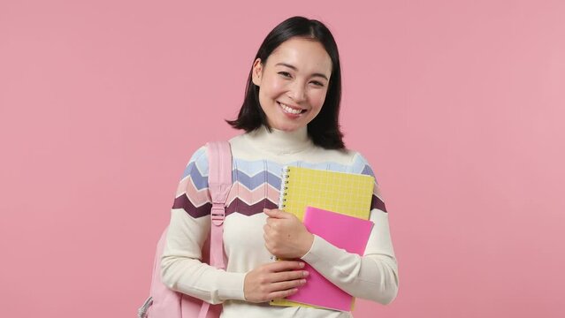 Girl teen student of Asian ethnicity 20s wears shirt backpack hold books look camera isolated on plain pastel light pink background studio portrait. Education in high school university college concept