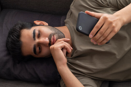 Portrait of a young man lying on sofa and looking at the Smartphone