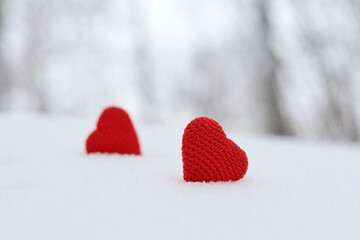 Love knitted hearts, Valentine's card, two red symbols of passion in the snow on forest background. Concept of romantic event, celebration or winter weather