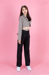 Portrait studio shot of Asian young urban trendy female hipster teenager fashion model in casual crop top street wears jacket holding sunglasses on head standing look at camera on pink background