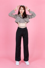 Portrait studio shot of Asian young urban trendy female hipster teenager fashion model in casual crop top street wears jacket holding sunglasses on head standing look at camera on pink background