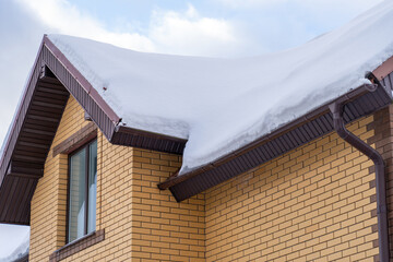house with new roof made of brown metal tiles and gutter covered with thick layer of snow in...